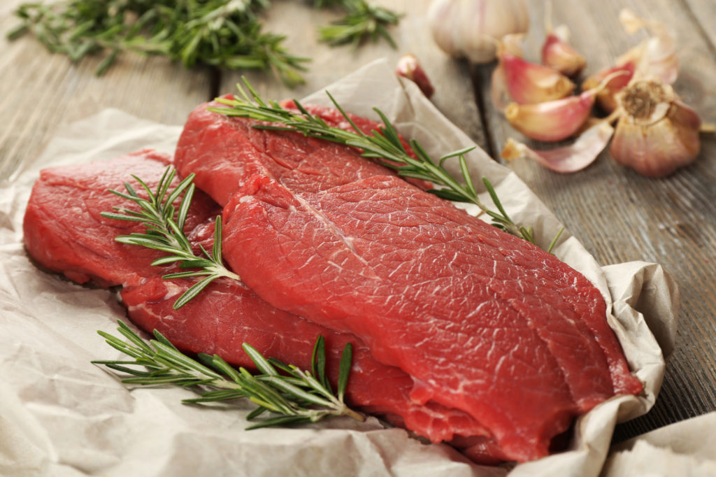 Raw Beef Steak With Rosemary And Garlic On Paper On Wooden Background
