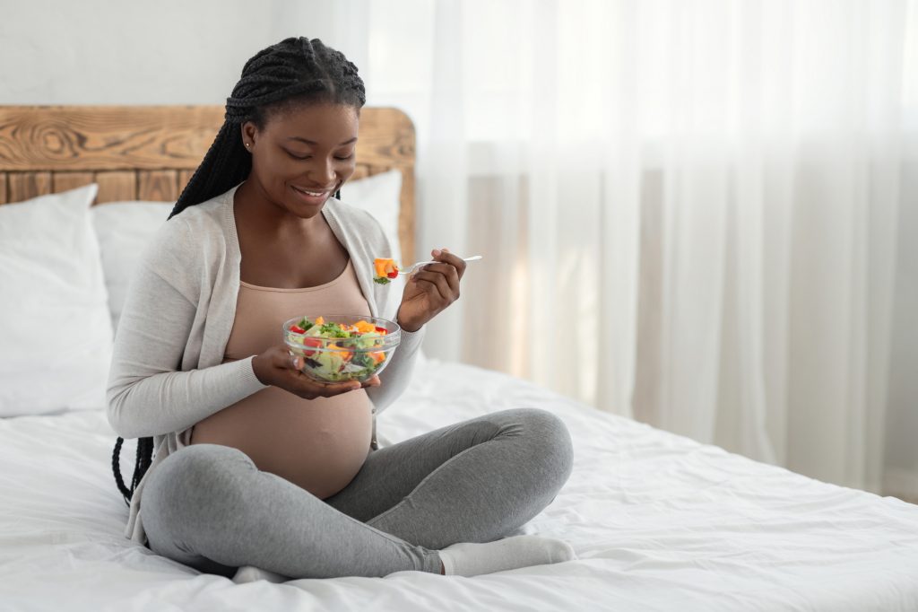 Pregnant Woman Nutrition. Happy Black Expecting Lady Eacting Vegetable Salad In Bed