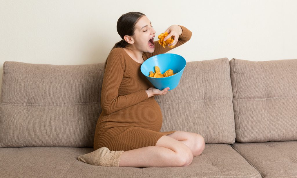 Pregnant Woman Is Eating Potato Chips Because Of Salt Cravings. Unhealthy Junk Food During Pregnancy Concept