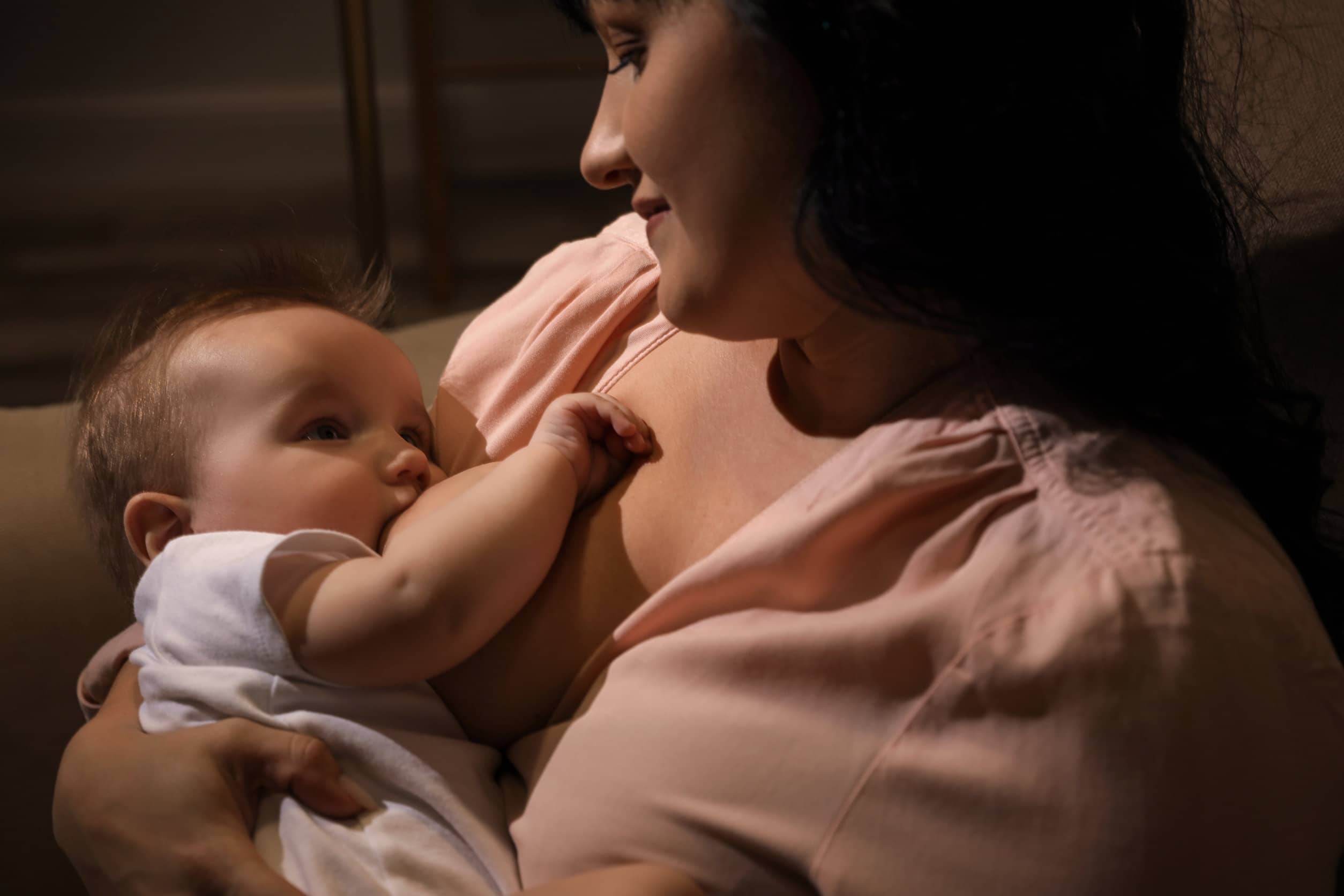 Woman Breastfeeding Her Little Baby On Sofa In Evening